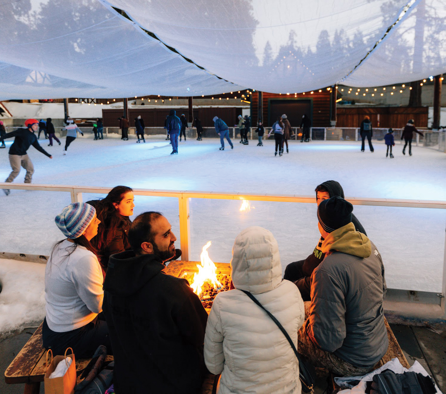A family sits around a fire pit in front of the ice skating rink.