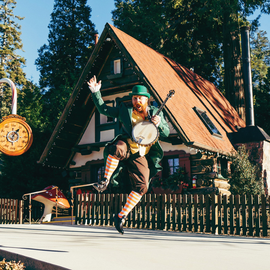 Seamus the Leprechaun leaps into the air while holding a banjo during Shamrocks & Shenanigans.